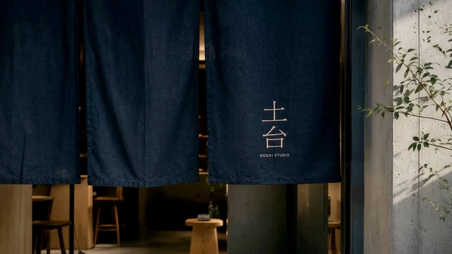 Noren marqué 土台 à l'entrée d'un lieu à Tokyo, tables et tabourets en bois derrière.